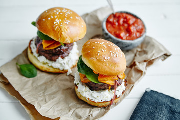 Burgers with grilled beef patties, cream cheese and spinach on classical bun. White wooden background