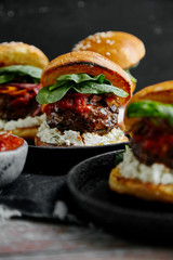 Burgers with grilled beef patties, cream cheese and spinach on classical bun. Dark rustic wooden background