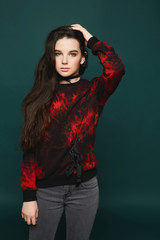 Young brunette teen model girl, in jeans and sweatshirt, posing at dark-green background