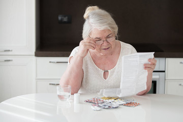  The grandmother in glasses reads the instruction on application of medicines. Many tablets on the table.