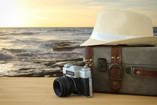 traveler vintage luggage, camera and fedora hat over wooden table infront of sunset landscape. holiday and vacation concept