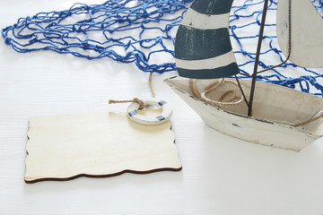 nautical concept image with white decorative sail boat and empty wooden board over white table.