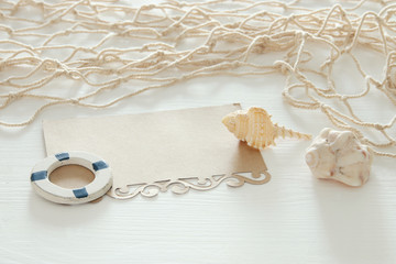 Fototapeta na wymiar nautical concept image with seashells, fish net and empty note over white wooden table.