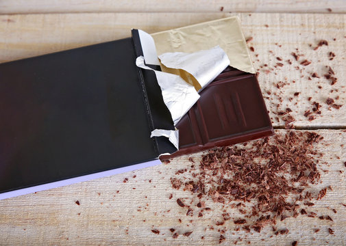 overhead studio shot of a dark chocolate bar in the package with shavings on a wooden background unhealthy food concept