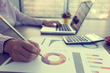 . Close-up hand writing on graph financial diagram document with pencil and another hand work on...