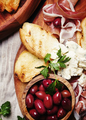 Snacks or antipasti, crostini, prosciutto, blue cheese and olives, black background, top view