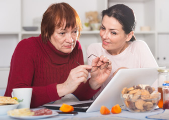 Woman at tea table using laptop with mature mother