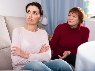 Sad mature female and daughter at sofa after quarrel