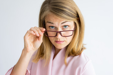 Frowning puzzled teacher looking surprised. Shocked displeased lady looking at camera over her glasses. Serious middle-aged woman wrinkling forehead and adjusting eyewear. Strictness concept