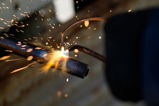 hands of man, using argon gas welding to weld metal pipe, sparks flying in all directions