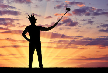 Silhouette of a narcissistic and selfish man with a crown on his head, makes selfie on the phone