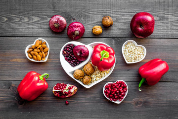 Proper nutrition for pathients with heart disease. Cholesterol reduce diet. Vegetables, fruits, nuts in heart shaped bowl on dark wooden background top view