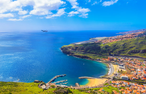 Aerial view of Machico bay in Madeira, with an airplane taking off against the ocean and the coastline of island in Portugal