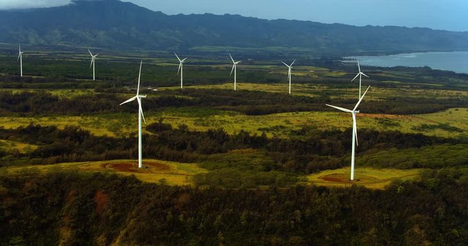 Aerial view of windmills spinning on sunny summer day in tropical forest environment 