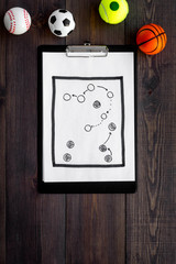Sport coach concept. Pad with tactic plan of the match near whistle and balls on wooden background top view copy space
