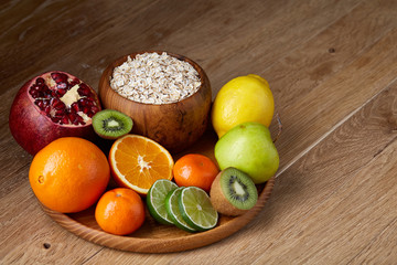 Bowl with oatmeal flakes served with fruits on wooden tray over rustic background, flat lay, selective focus