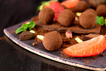 Chocolate truffles covered with cacao powder surrounded by strawberries and mint