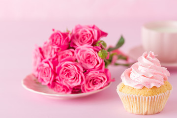 Cupcake with pink cream decoration and roses on pink pastel background.