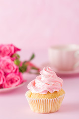 Cupcake with pink cream decoration and roses on pink pastel background.