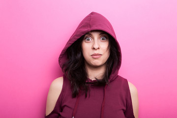 Woman wearing a hood makes silly faces at the camera on pink background in studio