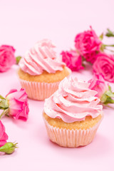 Cupcake with pink cream decoration and roses on pink pastel background.