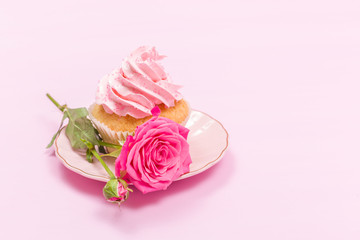 Cupcake with pink cream decoration and roses on pink pastel background.