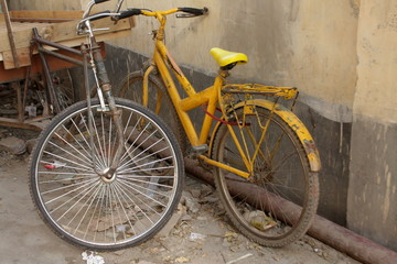 Fototapeta na wymiar Rusty Yellow bike and a tricycle van in-front a wall. Old memories of Cycling.