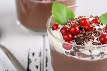 Chocolate mousse with currant and mint in a glasses on a whiite wooden background.