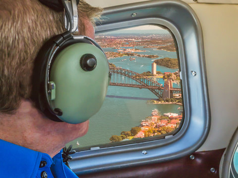 View From A Sea Plane Window Flying Over Sydney Harbour Australia. A Tourist Man Looks Out Wearing Ear Defenders.