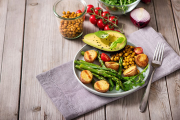 Healthy dinner with baked potatoes, green asparagus and spicy chickpeas, avocado, arugula, vegan,...
