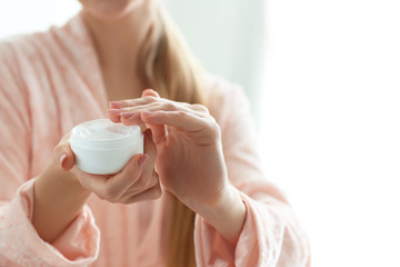 Young woman with jar of body cream at home