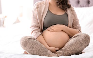 Young pregnant woman sitting on bed at home