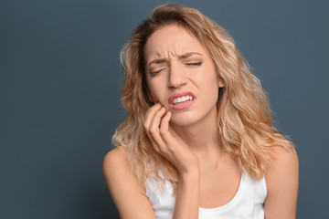 Young woman suffering from toothache on color background