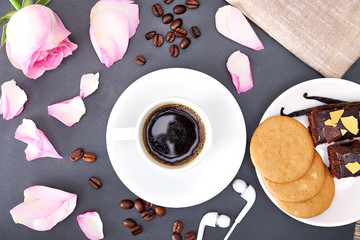 Roses, cookies and cup of coffee on black background. Flat lay