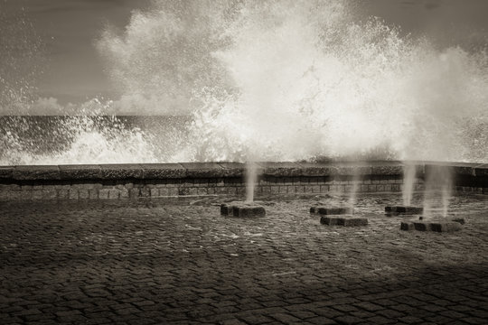 Fototapeta scenic view on vertical sprays of sea water waves passing through underground floor channels in san sebastian, spain in black and white sepia  