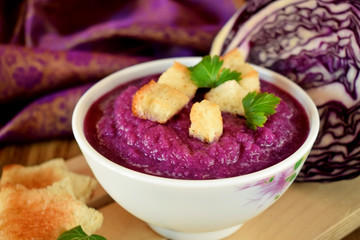 Cream soup made of red cabbage with croutons and parsley on wooden table