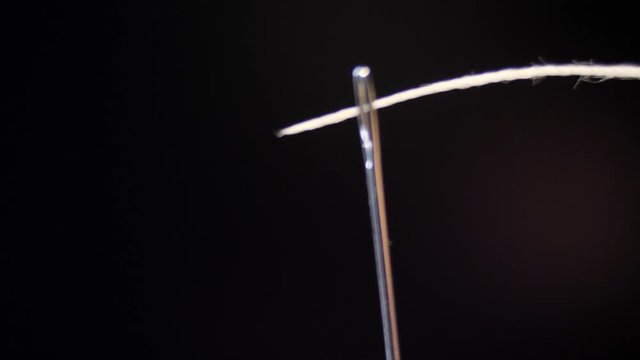 Threading the eye of a needle. Pulling the thread into the needle eye of the sewing needle.