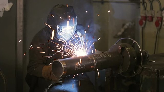 The working welder processes the metal, prepares the base. A man in a protective suit, sparks.