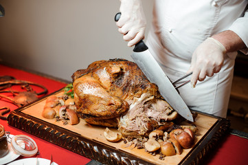 Professional cook cutting a whole roasted turkey on the wooden board