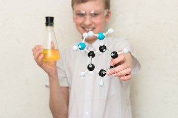 A teenager boy in a chemistry class holds a flask with chemicals and a plastic model of a molecule. Science. STEM education. School lab.