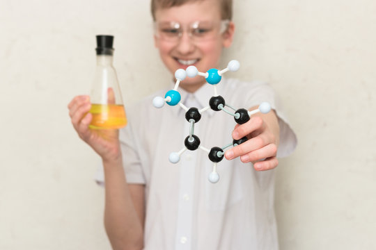 A teenager boy in a chemistry class holds a flask with chemicals and a plastic model of a molecule. Science. STEM education. School lab.