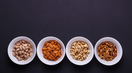Four bowls with different nuts on a black table