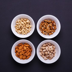 Four bowls with different nuts on a black table