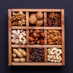 Assortment of nuts in a wooden box on a black background - healthy snack.