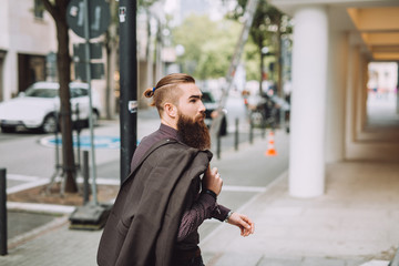 Obraz premium Young man with the beard goes on the street. on the back you stylish classic jacket