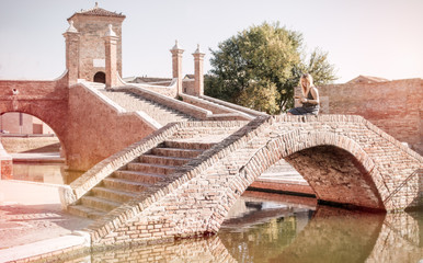 young female tourist in italy sitting on treponti bridge in comacchio medieval town