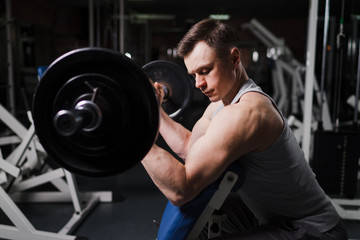Fototapeta na wymiar Strong handsome fit man exercising in the gym. Personal trainer workout. Athletic man working out his arms muscles with barbell on a bench. Fitness, healhty lifestyle, bodybuilding concept.