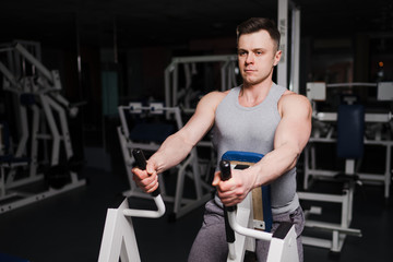 Naklejka na ściany i meble Strong handsome fit man exercising in the gym. Personal trainer workout. Athletic man working out his arms and chest muscles. Fitness, healhty lifestyle, bodybuilding concept.