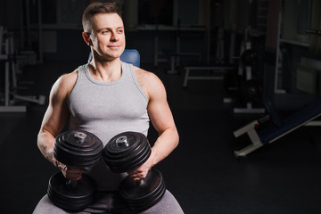 Fototapeta na wymiar Strong handsome fit man exercising in the gym. Personal trainer workout. Athletic man working out his chest with dumbbells on a bench. Fitness, healhty lifestyle, bodybuilding concept.