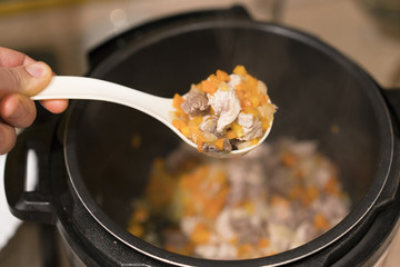 Cooked meat with vegetables in a cooked white spoon on a steam background